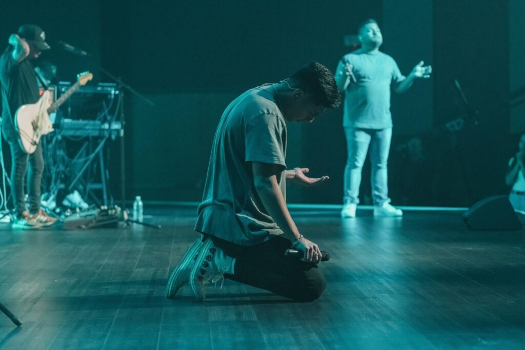 Man kneeling on stage holding microphone in worship